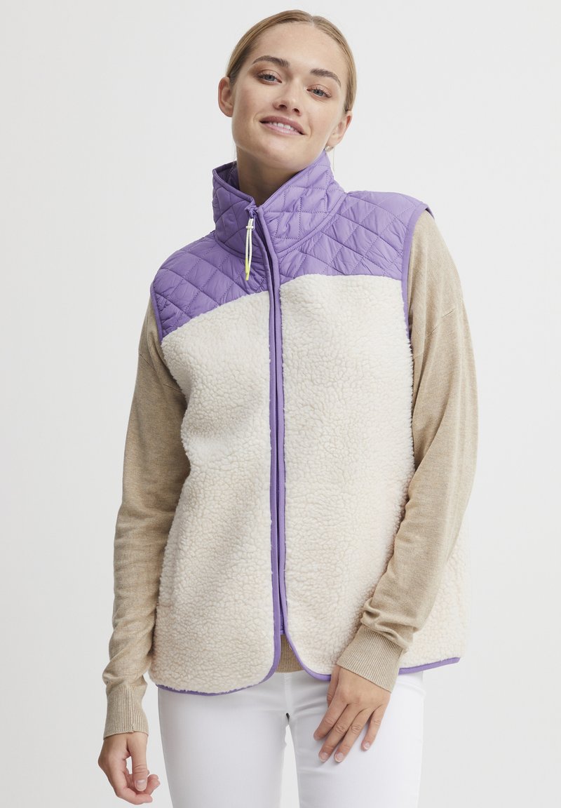 Vesta matlasată cu partea superioară mov și partea inferioară din fleece crem, având un guler înalt, închidere cu fermoar și detalii de trim violet.