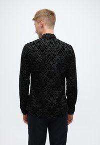 Must pikkade varrukatega särk, millel on tekstureeritud ja reljeefne lillemuster. Kitsas lõige, kõver äärejoon ja nööbitavad varrukapöörad. Pehme sametmaterjal.