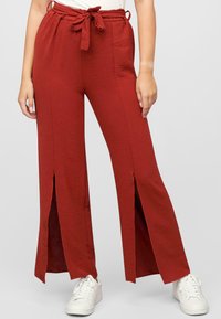 Pantaloni larghi rossi con un tessuto strutturato, caratterizzati da fessure frontali e una vita con cordino. Abbinati a sneakers bianche.
