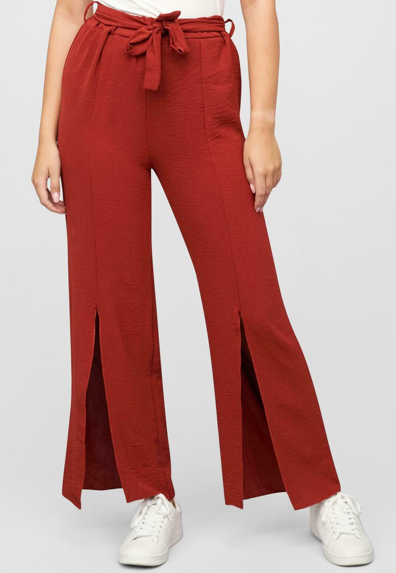 Pantaloni larghi rossi con un tessuto strutturato, caratterizzati da fessure frontali e una vita con cordino. Abbinati a sneakers bianche.