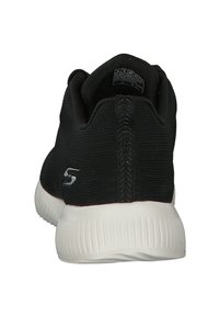Black athletic shoe with woven textile upper and white rubber outsole. Features a textured back with a prominent logo and stitched detailing.