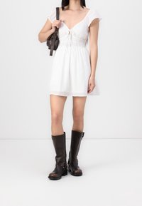 Vit klänning med korta puffärmar, smockad midja och knappdetalj. Matchad med bruna knälånga läderstövlar och en liten svart väska.