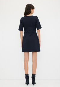 Abito navy con maniche corte, corpino aderente e gonna svasata. Tessuto liscio e design minimalista con chiusura a cerniera sul retro.