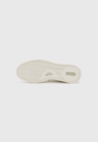 White sneaker sole with a herringbone pattern, featuring a light green accent and a smooth surface. Designed with a rounded toe and cushion support.