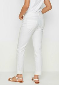 Pantalones de mezclilla blanca con corte recto, dobladillos ajustados y dos bolsillos traseros, combinados con sandalias ligeras sobre un fondo neutro.