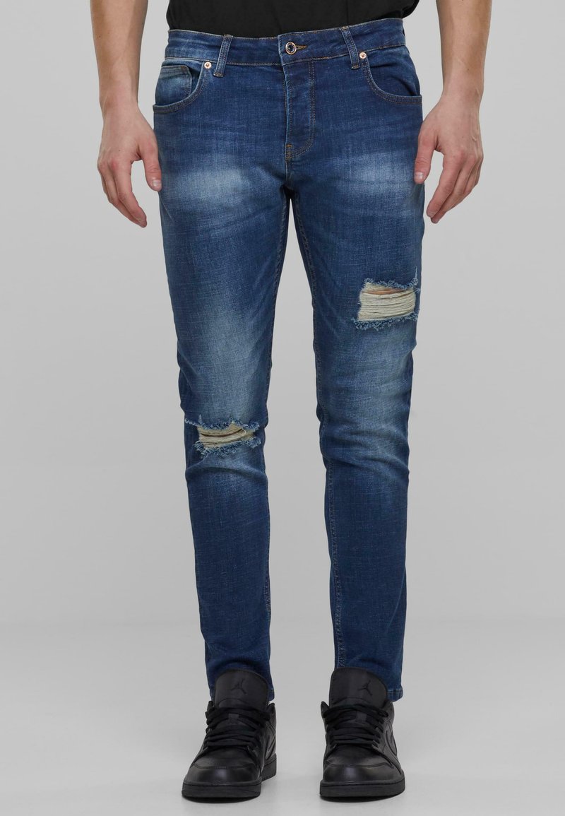 Tummansiniset farkut slim fit -mallissa, joissa on kuluneita laikkuja polvissa ja hillittyä haalistumista reidissä.