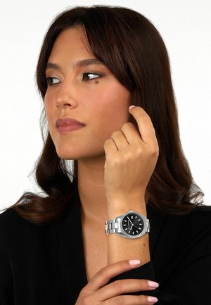 Silberner Edelstahl-Armbanduhr mit schwarzem Zifferblatt und silbernen Akzenten, ausgestattet mit einem runden Gehäuse, einem Metallarmband und einer Datumsanzeige.