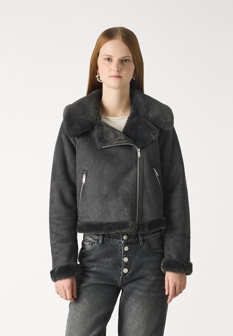 Veste cropped en faux suède gris avec un large col en fourrure et des poignets, dotée de deux poches avant zippées et d'accents en métal.