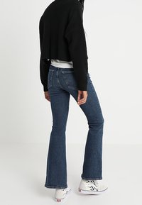 Tmavě modré rozšířené džíny s klasickou denimovou texturou, doplněné černým zkráceným svetrém a bílými teniskami s potiskem.