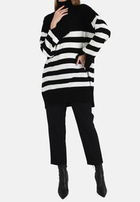 Pull col roulé surdimensionné à rayures noires et blanches avec manches longues, associé à un pantalon noir ajusté et des bottines pointues.