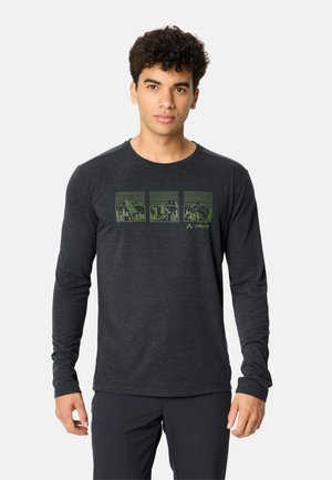 Uomo con capelli ricci che indossa una maglietta a maniche lunghe grigio scuro con tre grafiche verdi di paesaggi e il logo Vaude sul petto.