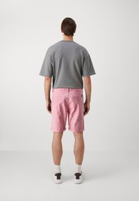 Grå kortermet skjorte med løs passform, parret med rosa oppbrettede shorts. Hvite sneakers med mørke detaljer. Enkel og avslappet design.