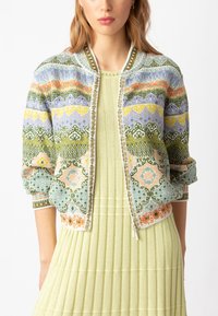 Megztas bomberio tipo švarkas su daugiaspalviais geometriniais raštais, žaliais, oranžiniais ir geltonais akcentais. Minkšta tekstūra ir aiki mynlygumui. Uždarymas užtrauktuku.