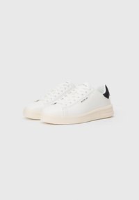 Adidași din piele albă cu talpă plată, accente negre pe toc și design cu șireturi. Logo-ul mărcii tipărit pe lateral. Textură netedă.