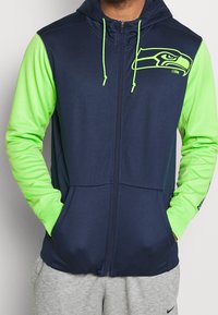 Navy blue zip-up hoodie with bright green sleeves and accents. Features a Seattle Seahawks logo on the chest and drawstring hood.