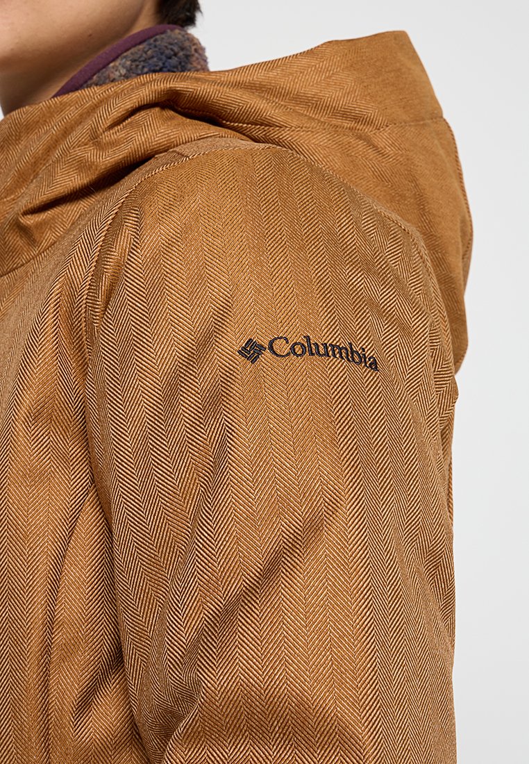 Braune Jacke im Fischgrätenmuster mit Kapuze, mit einem schwarzen Columbia-Logo. Texturiertes Material mit sichtbaren Nähten.