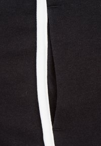 Svart tyg med en vit rand längs den ena sidan, som har en mjuk textur och en lätt stretch, vilket betonar en avslappnad, sportig design.