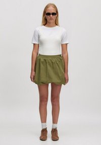 Witte aansluitende top met korte mouwen, gelaagd onder een groene, geraffineerde rok. Bruine veterschoenen en witte sokken maken de outfit compleet.