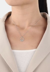 Silver necklace with a round pendant featuring two figures, set against a light background. The chain is delicate and thin.