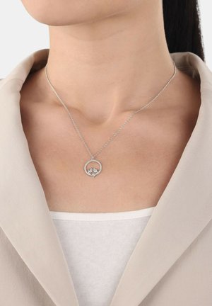 Collana d'argento con un pendente rotondo che presenta due figure, su uno sfondo chiaro. La catena è delicata e sottile.