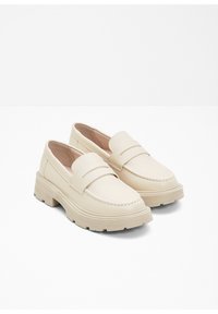 Mocassins en cuir beige avec un bout rond, des coutures décoratives et une épaisse semelle en caoutchouc. Présentent une large sangle sur le coup de pied.