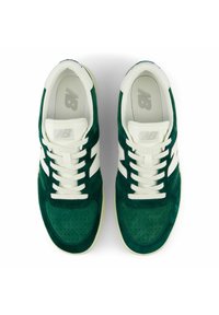 Vihreät mokkanahkaiset tennarit, joissa valkoiset korostukset, rei'itetty kärki, litteät nauhat ja kuvioitu pohja. Logo näkyy kielen kohdalla.