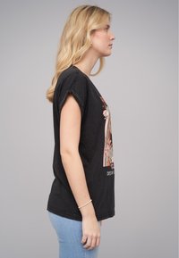 T-shirt noir avec des manches retroussées arborant un design graphique floral avec du texte, associé à un jean bleu clair. Tissu en coton doux.