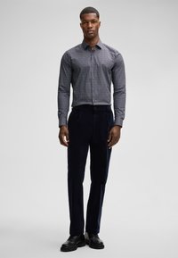 Pantaloni in corduroy blu navy abbinati a una camicia aderente con bottoni in un piccolo motivo a pois bianchi e blu navy. Scarpe nere solide completano il look.