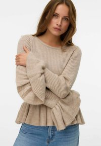 Maglione beige a coste con maniche a sbuffo e orlo inferiore plissettato, realizzato in un morbido materiale testurizzato. Abbinato a jeans in denim blu.