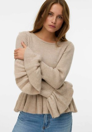 Pull en beige à côtes avec des manches évasées et un ourlet inférieur plissé, fabriqué en matière douce et texturée. Assorti à un jean en denim bleu.