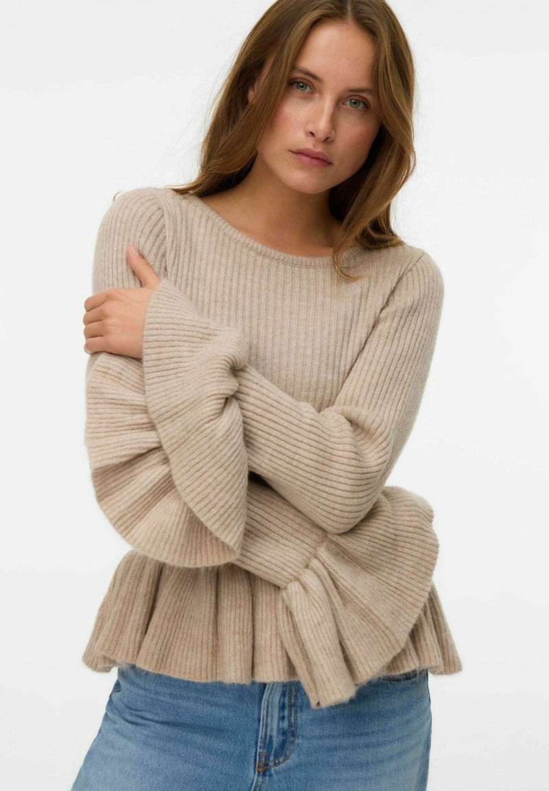 Maglione beige a coste con maniche a sbuffo e orlo inferiore plissettato, realizzato in un morbido materiale testurizzato. Abbinato a jeans in denim blu.