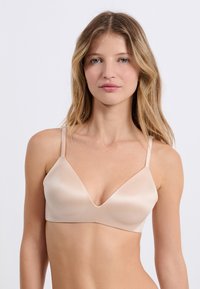 Soutien-gorge sans armatures en tissu doux couleur nude. Présente un décolleté plongeant en V, des bretelles fines et réglables, et une texture lisse et mate.