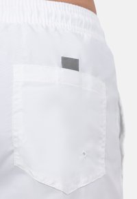 Pantaloni corti bianchi con vita elastica, dotati di una tasca posteriore quadrata con un accento grigio. Il tessuto ha una texture liscia e leggera.