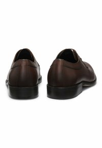 Scarpe in pelle marrone con finitura liscia, punta rotonda e dettagli cuciti. Tacco basso e suola nera testurizzata. Vista di profilo dal retro.