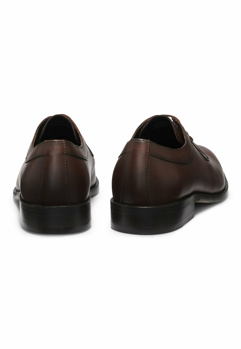 Chaussures en cuir marron avec une finition lisse, bout rond et détails en couture. Petit talon et semelle noire texturée. Vue de profil par l'arrière.