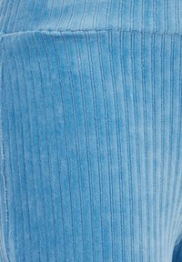 Svjetloplavi kordura materijal s vertikalnom rebrastom teksturom. Materijal je mekan i pufnast, s ravnomjerno razmaknutim linijama koje se protežu duž površine.