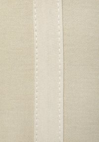 Smėlio spalvos audinys su lygiu paviršiumi turi vertikalią siūlę ir kontrastingą siuvinėjimą. Šiek tiek tamsesnis audinys šalia siūlės.