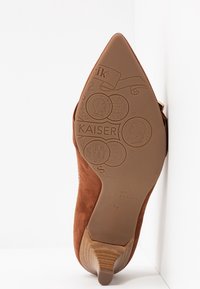 Semelle en suède brun à talons hauts avec logos embossés et motifs décoratifs. Bout pointu et accent en bois sur le talon.