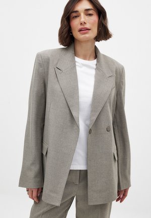 Szary dwurzędowy żakiet z teksturowanej tkaniny, z szerokimi klapami, kieszeniami bocznymi i luźnym krojem, w zestawie z białym t-shirtem pod spodem.