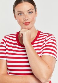 Rood-wit gestreept t-shirt met een ronde halslijn, korte mouwen en ribbelstructuur, gedragen door een persoon met gevouwen armen.