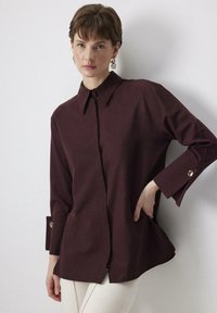 Camicia button-up bordeaux con colletto, maniche lunghe con polsini abbottonati e vestibilità rilassata; realizzata in tessuto morbido, con dettagli di cucitura minimi.