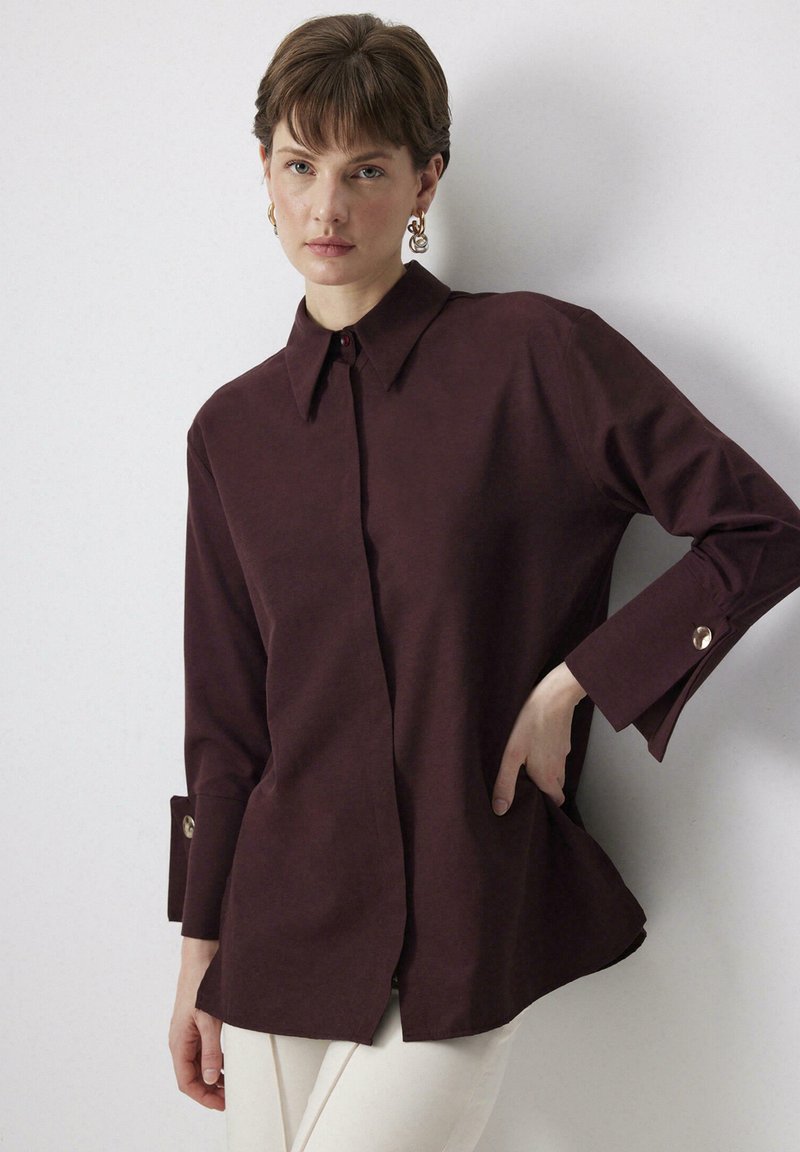 Camicia button-up bordeaux con colletto, maniche lunghe con polsini abbottonati e vestibilità rilassata; realizzata in tessuto morbido, con dettagli di cucitura minimi.