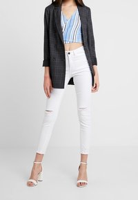 Blazer de cuadros gris, top corto a rayas azules, jeans skinny blancos desgastados y sandalias de tacón blancas. Enfócate en los materiales y el ajuste.