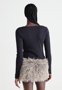 Zwarte langemouwen top met een vierkante halslijn, gecombineerd met een korte, gestructureerde grijze bontrok. De outfit heeft zachte, pluffige accenten.