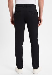 Black slim-fit trousers with a textured fabric, featuring a classic waistband and two back pockets, paired with white sneakers.