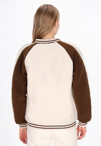 Kurtka z polaru z kremowym korpusem i brązowymi raglanowymi rękawami, z prążkowanym kołnierzem i mankietami w brązowe i białe paski. Miękka tekstura.