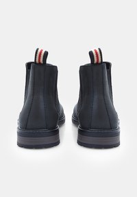Cizme Chelsea din piele neagră, cu laturi elastice, talpă rezistentă și inserții cu dungi roșii și albe. Textură netedă cu un finisaj mat.