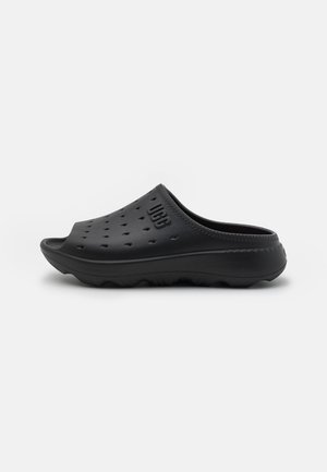 Zuecos negros sin cordones de material suave, con agujeros de ventilación, punta redondeada y suela texturizada para mayor agarre.