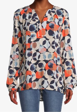 Blouse à manches longues avec col en V, avec un motif abstrait multicolore de cercles en marine, orange, bleu et beige, associée à un jean bleu.