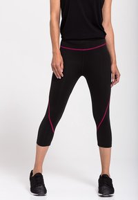 Leggings capri neri con dettagli rosa lungo le cuciture, realizzati in un materiale elastico. Abbinati a scarpe sportive nere e a una maglietta attillata.